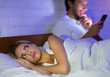 Man Texting On Mobile Phone Lying In Bed With Wife