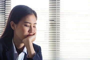 Young Asian woman working at her desk in the office looking at laptop with boring face due to work load and difficulty in dealing with customers. Feeling tired and lazy lack of motivation at work