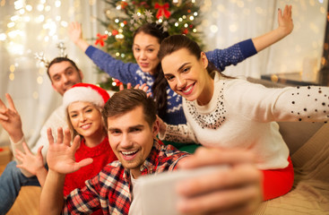 Wall Mural - celebration and holidays concept - happy friends with glasses celebrating christmas at home party and taking selfie by smartphone