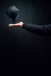 Isolated hand balancing black urban hat, black hoodie, hand on a black background