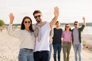 Wall Mural - friendship, leisure and people concept - happy couple with group of friends on beach in summer waving hands