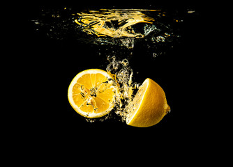 Fresh yellow lemon halves in water splash on black background with lots of air bubbles.