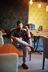 Wall Mural - Confident young indian man in black shirt sitting at cafe.