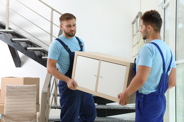 Wall Mural - Professional workers carrying cabinet at stairs in office. Moving service