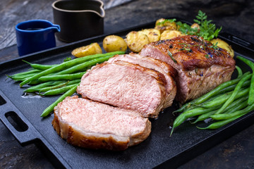 Traditional roasted dry aged veal tenderloin with beans and potatoes offered as closeup on a modern design cast iron tray