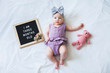 Three months old baby girl laying down on white background with letter board and teddy bear.
