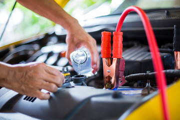 Wall Mural - Hands of mechanic check water in yellow car radiator and add water to car radiator with charging car battery with electricity trough cables. Service and maintenance vehicles, Selective focus.