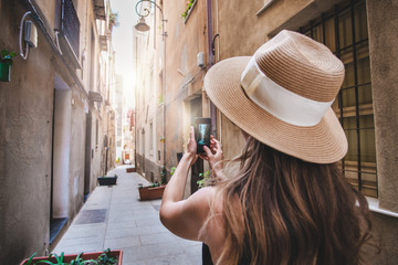 Girl backpacker taking photo on her mobile phone while walking on the old town narrow street