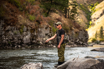 Wall Mural - Fly fisherman casting in the mountain stream during the fall season.