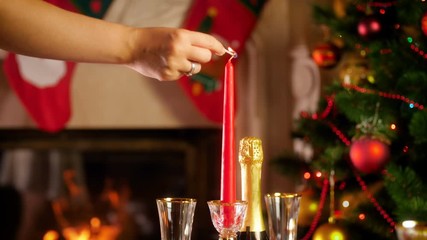 Wall Mural - 4k footage of female hand lighting up candle with matches against burning fireplace and glowing Christmas tree. Dining table served for big family on winter holidays and celebrations.