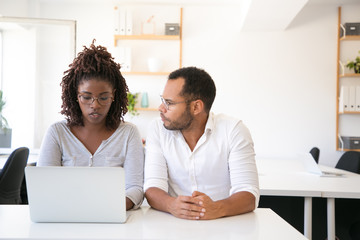 Trainer explaining corporate project specifics to intern. Business man and woman in casual sitting at workplace, using laptop and talking. Corporate training concept