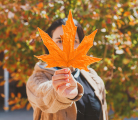 Wall Mural - Fall season concept. Beautiful middle-eastern woman holds an yellow autumn leaf