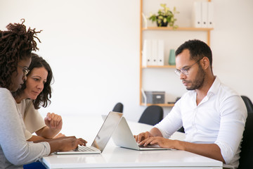 Wall Mural - Diverse business team meeting and working on project together. Man and women in casual sitting at table and using laptops. Working together concept