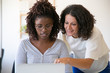 © Mangostar - Diverse female coworkers working on computer together. Business women sitting and standing at workplace, using laptop, pointing at screen, smiling. Corporate teaching concept