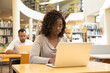 © Mangostar - Serious African American student working on research paper in library. People sitting at desks and using laptops in computer class with bookshelves. Academic research concept