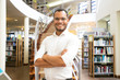 © Mangostar - Smiling African American man posing at public library. Front view of confident young guy with crossed arms standing in front of stairs. Knowledge concept