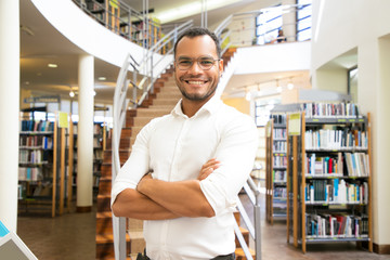 Smiling African American man posing at public library. Front view of confident young guy with crossed arms standing in front of stairs. Knowledge concept