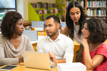 Excited colleagues discussing some questions at library. Four mature students working with laptop together. Education concept