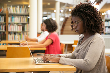Wall Mural - focused female customer using public wi-fi hotspot in library. young african american woman sitting 