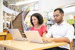 © Mangostar - Focused college students taking online test in library. Man and woman in casual sitting at desk, using laptops, typing. Online exam concept