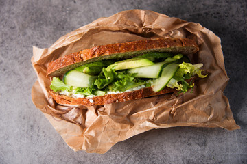 Wall Mural - Healthy sandwich with green ingredients, avocado, cucumber and salad. Wrapped in brown paper. Gourmet conception.