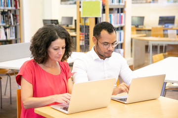 Wall Mural - focused trainees taking tests in classroom. man and woman in casual sitting at desk, using laptops, 