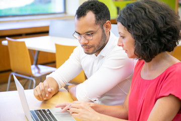 Wall Mural - coworkers doing research in library. man and woman in casual sitting at desk, using laptop and talki