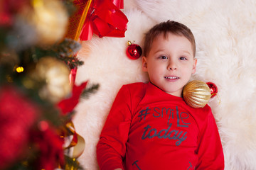 cute five year old boy in red pajamas having fun under the Christmas tree, top view