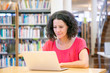 © Mangostar - Serious excited female user working on computer in library. Focused middle aged Caucasian woman in casual sitting at desk, using laptop, watching content. Bookshelves in background. Library concept