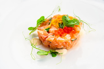 Fresh and tasty tartare of raw salmon prepared with salmons eggs and vegetables on top served in white plate