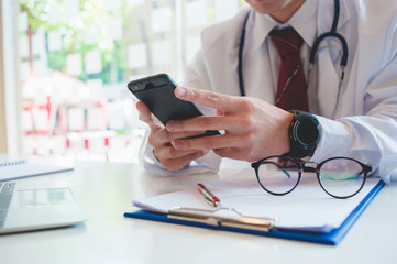 An Asian doctor is using a smartphone on a white desk at a hospital. Intelligent Health Technology Concepts