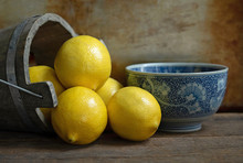 Original Textured Still Life Photograph Of Lemons Pouring Out Of A Wooden Bucket With A Blue China Bowl On Brown