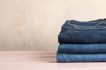 Wall Mural - Stack of jeans pants on light pink background, space for text