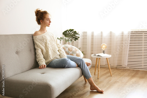 Photographie Young beautiful woman wearing white sweater on grey textile sofa at home