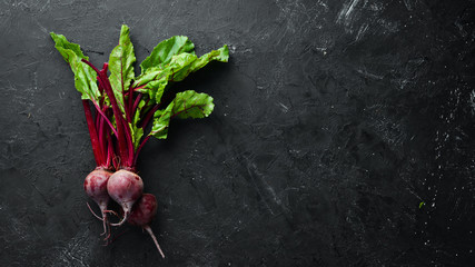 Wall Mural - Fresh beetroot with leaves on a black stone background. Healthy food. Top view. Free space for your text.