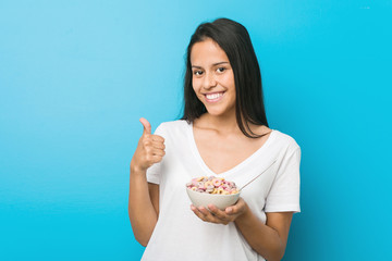 Young hispanic woman holding a sugar cereal bowl smiling and raising thumb up