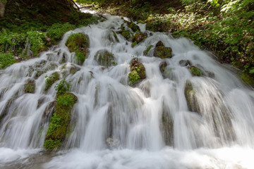 Waterfall rushing down a steep hill in a forest.