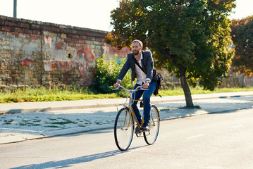 Bearded Businessman in business suit riding on retro bicycle to work on urban street in the morning on sunset