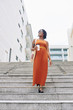 © DragonImages - African beautiful woman in long orange dress drinking coffee and moving down the stairs in ancient city