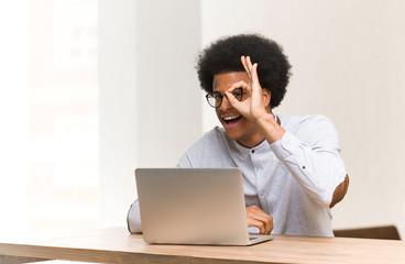 Wall Mural - Young black man using his laptop confident doing ok gesture on eye