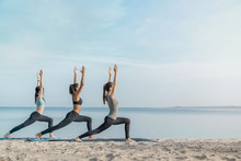 Full Length Image Of Young Multiethnic Group Of Woman Practicing Yoga Exercise At The Beach Near Water