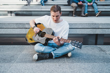 Musician Looking At The Guitar Sitting On The Floor With People Behind