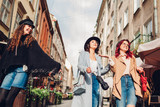 Fototapeta Miasto - Girls talking and having fun. Outdoor shot of three young women walking on city street.