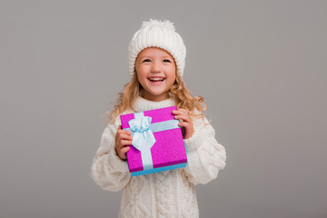 Wall Mural - little blonde girl in winter white winter hat smiling holding a pink gift box