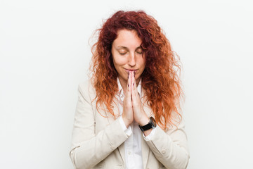 Young natural redhead business woman isolated against white background holding hands in pray near mouth, feels confident.