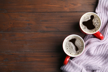 Flat lay composition cups of hot coffee and knitted sweater on wooden background, space for text. Winter drink