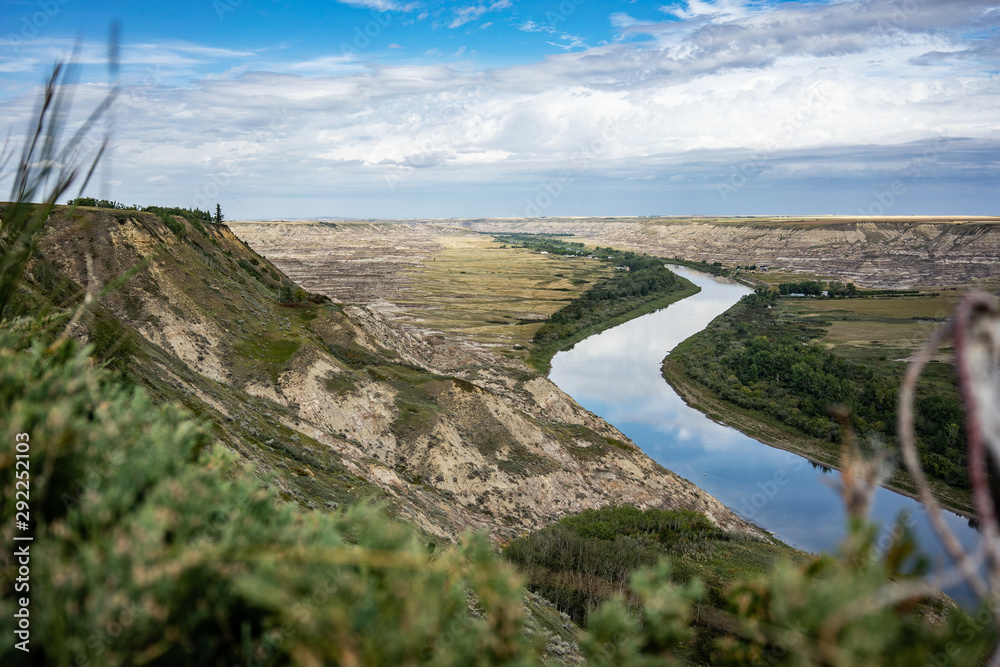 Reflective river cutting through the Alberta Badlands with exposed ...