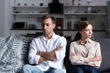 Wall Mural - pensive sad man and woman sitting on sofa with crossed arms