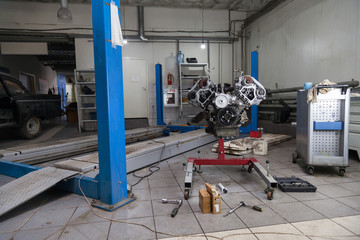 Used v8 engine mounted on a crane for installation on a car after a breakdown and renew in a vehicle repair workshop as a guarantee for the dealership. Auto service industry.