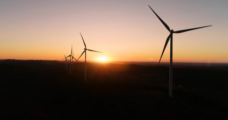 Wind turbines under the orange sunset. This is a wind farm which produce sustainable energy, perfect for the environment - aerial view with a drone - environmental & ecological concept